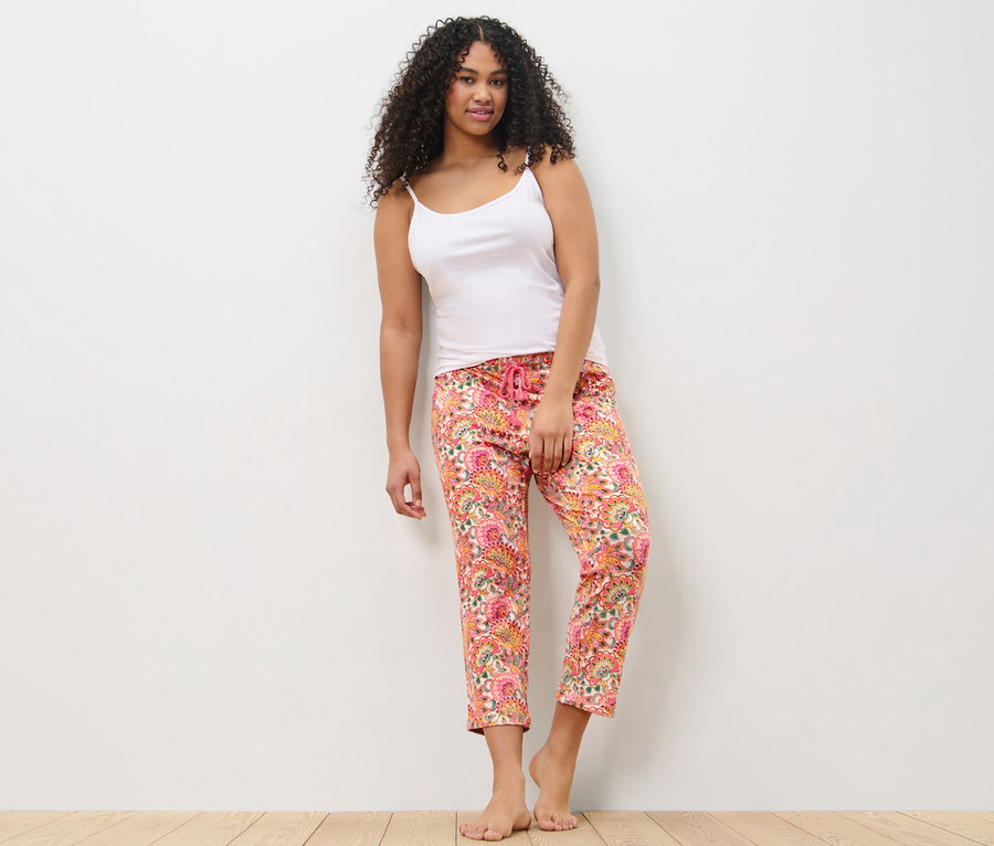 Frau lehnt an einer Wand und trägt eine Pyjamahose und ein Tanktop.