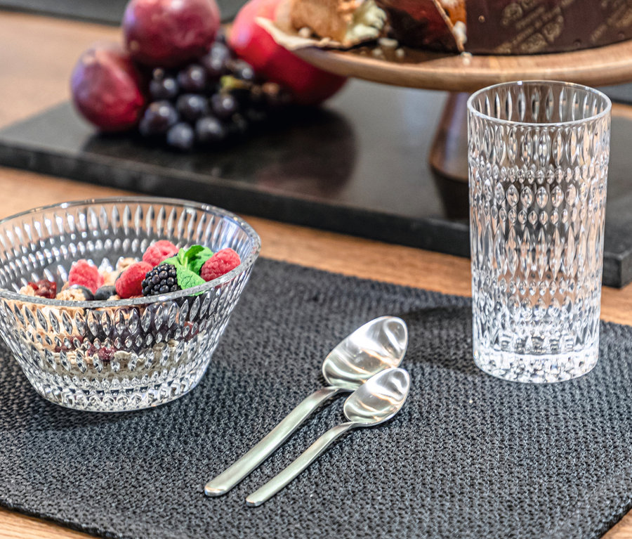 Nahaufnahme einer Schüssel Müsli mit Früchten, zwei Löffeln und einem Nachtmann Longdrinkglas »Ethno« auf einem grauen Tischset.