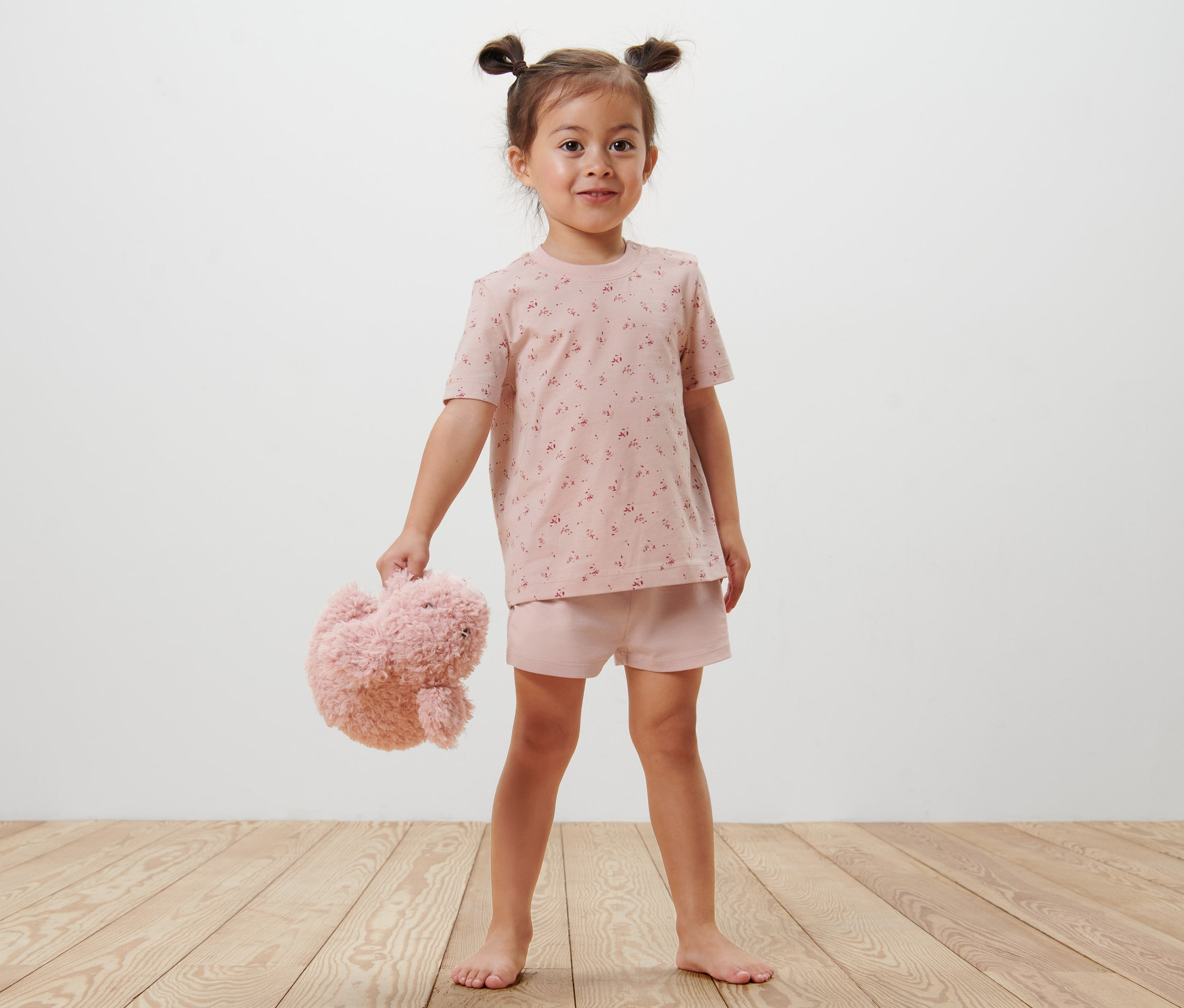 Mädchen steht barfuß und hält Teddy, trägt kurzen Blümchen-Pyjama.