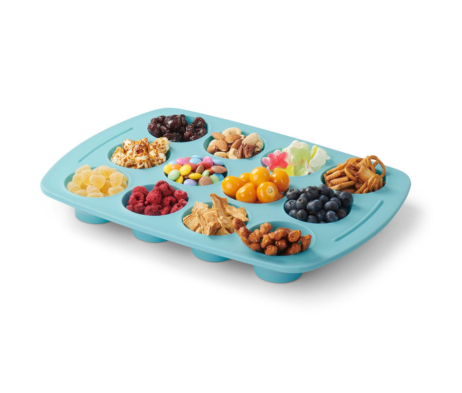 Ein faltbares Silikon-Muffinblech gefüllt mit Rosinen, Popcorn, Bonbons, Nüssen, Gummibärchen, Brezeln, kandierten Früchten, Himbeeren, Getreide, Physalis, Blaubeeren und Erdnüssen.