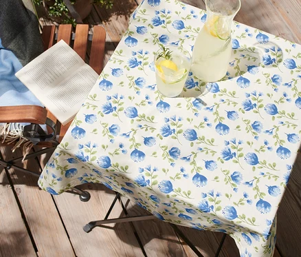 Auf einem Tisch auf einer Terrasse liegt eine abwischbare Tischdecke, ca. 90 x 90 cm, mit blauen Blumen.