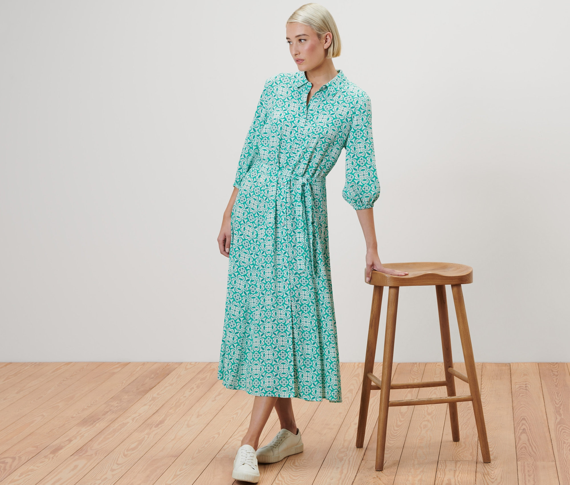 Frau posiert neben einem Holzhocker und trägt ein Hemdblusenkleid mit Alloverprint.