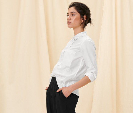 Frau posiert in weißer Hemdbluse und schwarzer Hose.