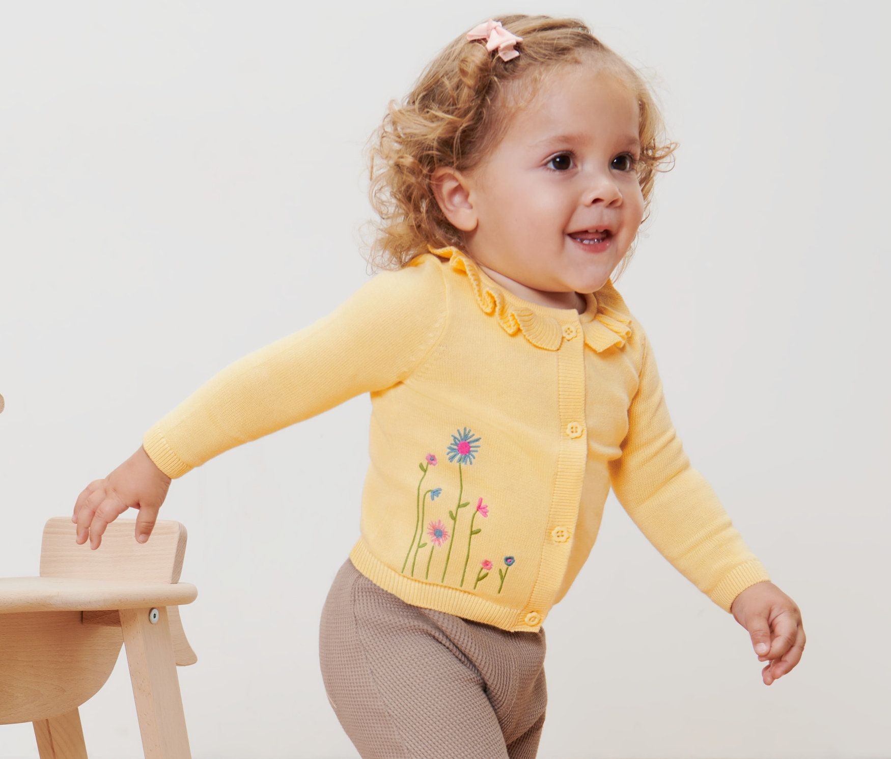 Ein Kind mit einer gelben Baby-Strickjacke steht neben einem hölzernen Schaukelpferd.