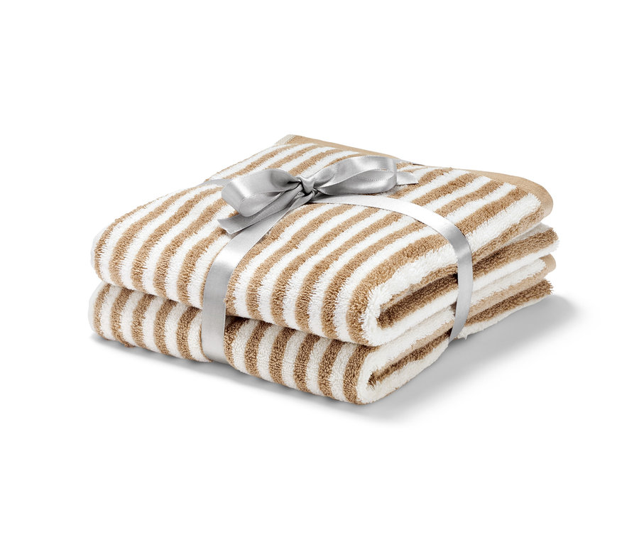 Zwei Premium-Handtücher, naturweiß und beige, mit silberner Schleife gebunden.