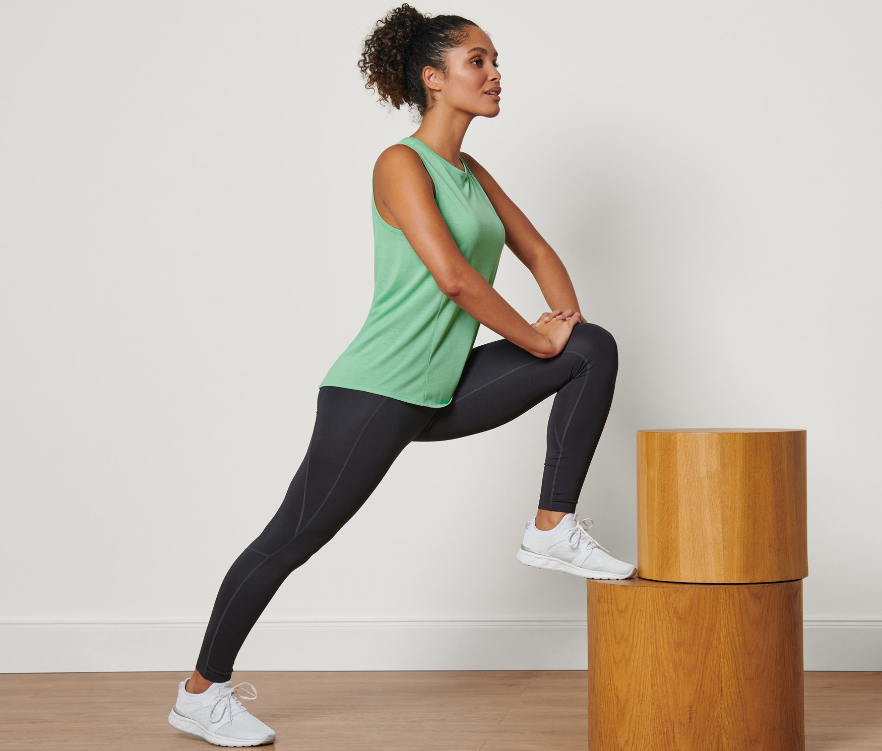 Frau dehnt sich auf Holzstufen und trägt ein grünes Sportoberteil.