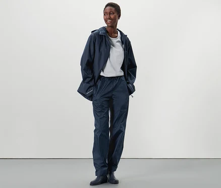 Eine Afroamerikanerin steht und trägt eine Unisex-Regenhose und eine Regenjacke.