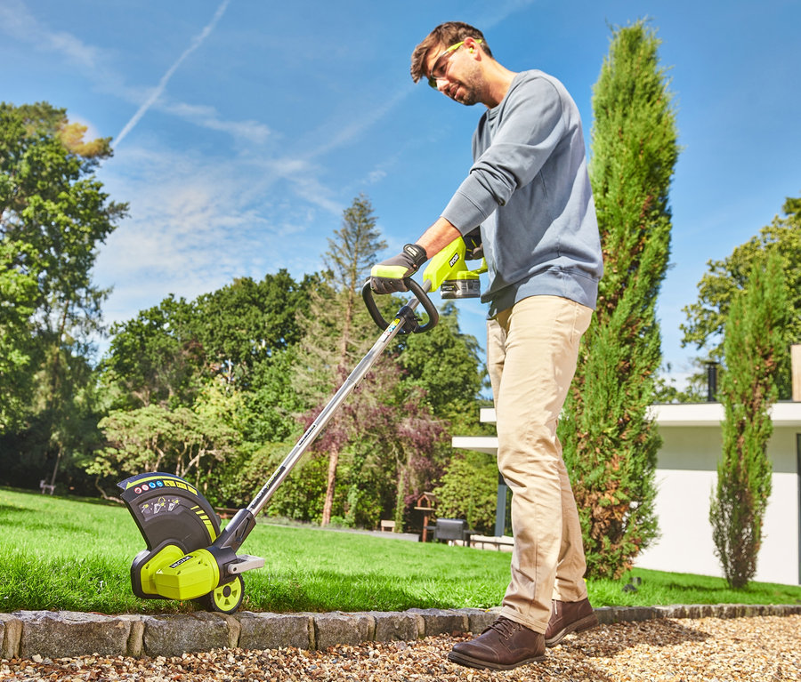 Ein Mann in beigen Hosen benutzt einen RYOBI 18 V One+ Akku-Rasentrimmer mit Radführung in einem Garten.