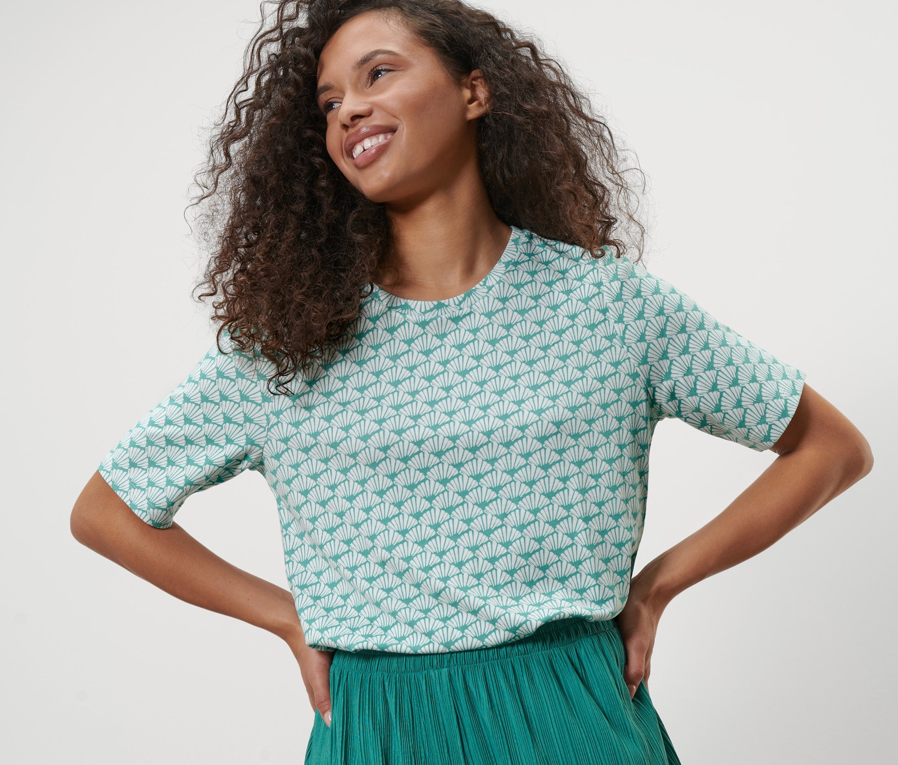Frau posiert in Interlock-Shirt mit Muschelmuster und grüner Hose.