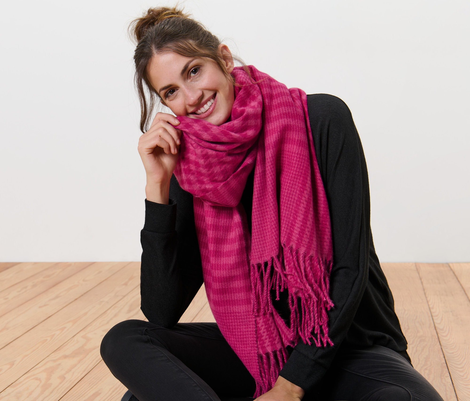 Eine Frau sitzt mit gekreuzten Beinen auf dem Boden und trägt einen Webschal mit Fransen.