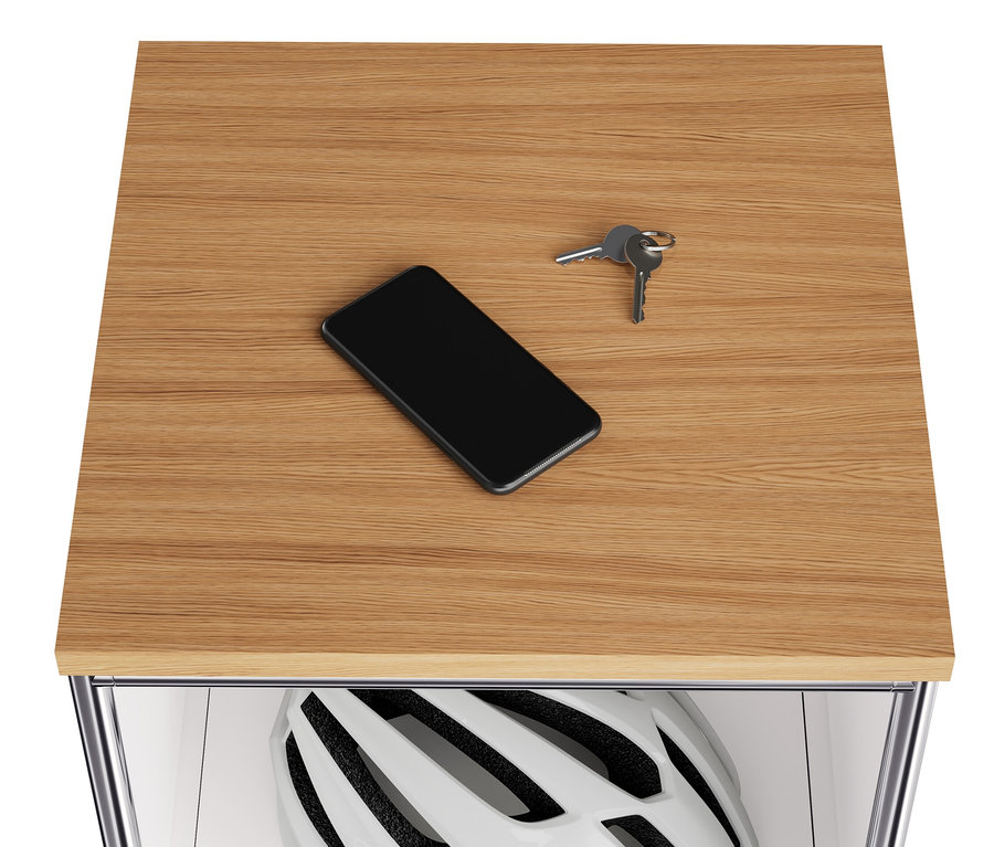 Auf der Holzplatte einer schmalen, weißen Metallkommode »CN3« liegen ein Handy und Schlüssel. Im Klappfach befindet sich ein Helm.