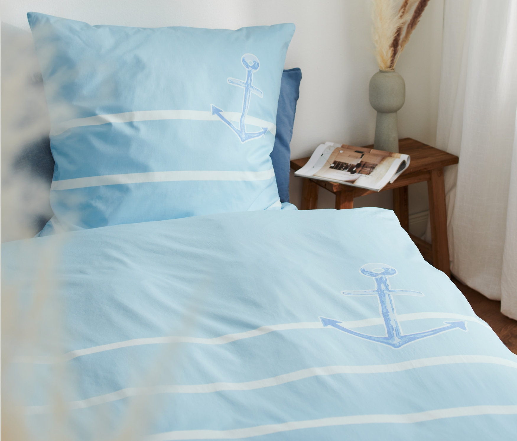 Hellblaue, gestreifte Premium-Baumwoll-Bettwäsche mit Ankermotiv auf einem Bett.