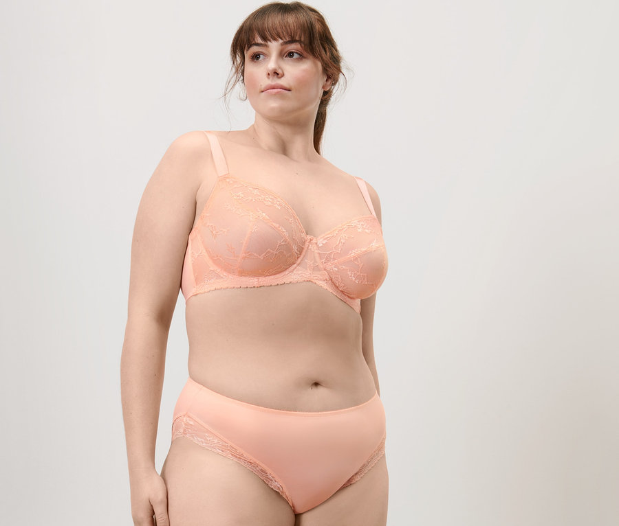 Frau posiert in apricotfarbenem Bügel-BH mit Spitze und Midrise-Slip.
