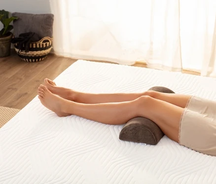 Frau liegt mit TEMPUR® Beinkissen auf einem Bett.