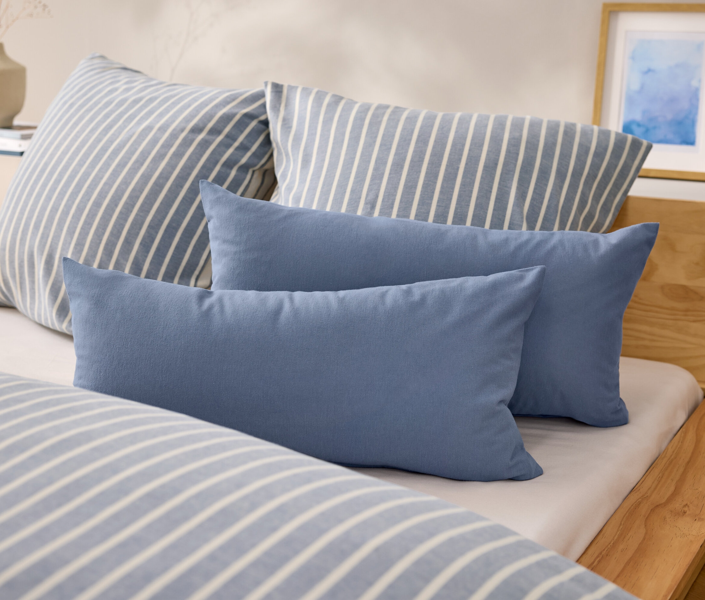 Auf einem Bett liegen zwei blaue, rechteckige Kissen und zwei Kissen mit blau-weißen Streifen.