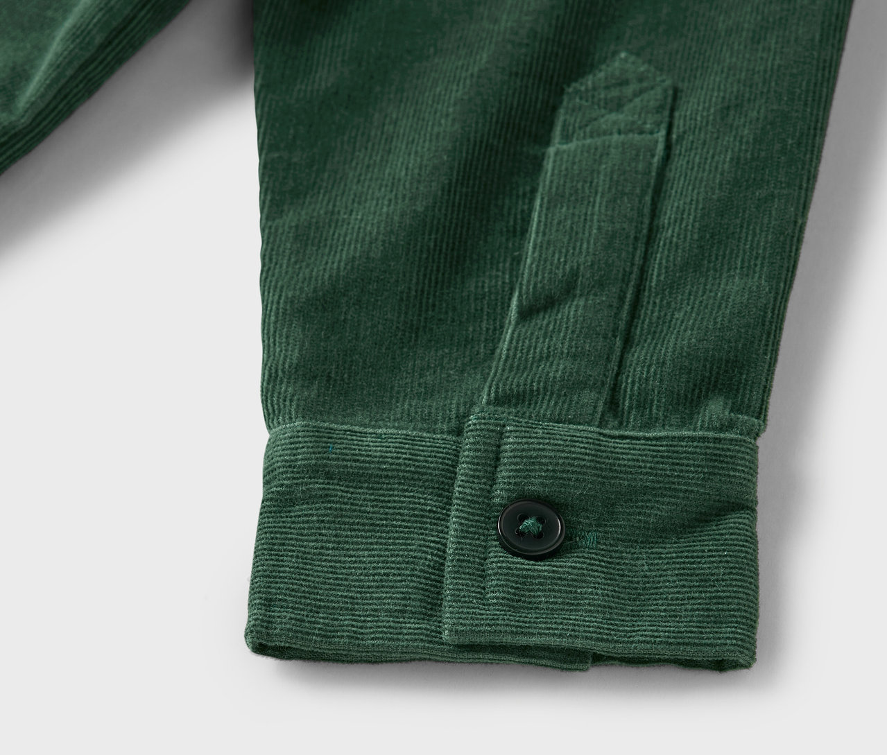 Detailaufnahme eines grünen Cordhemdes mit Knopf am Ärmel.