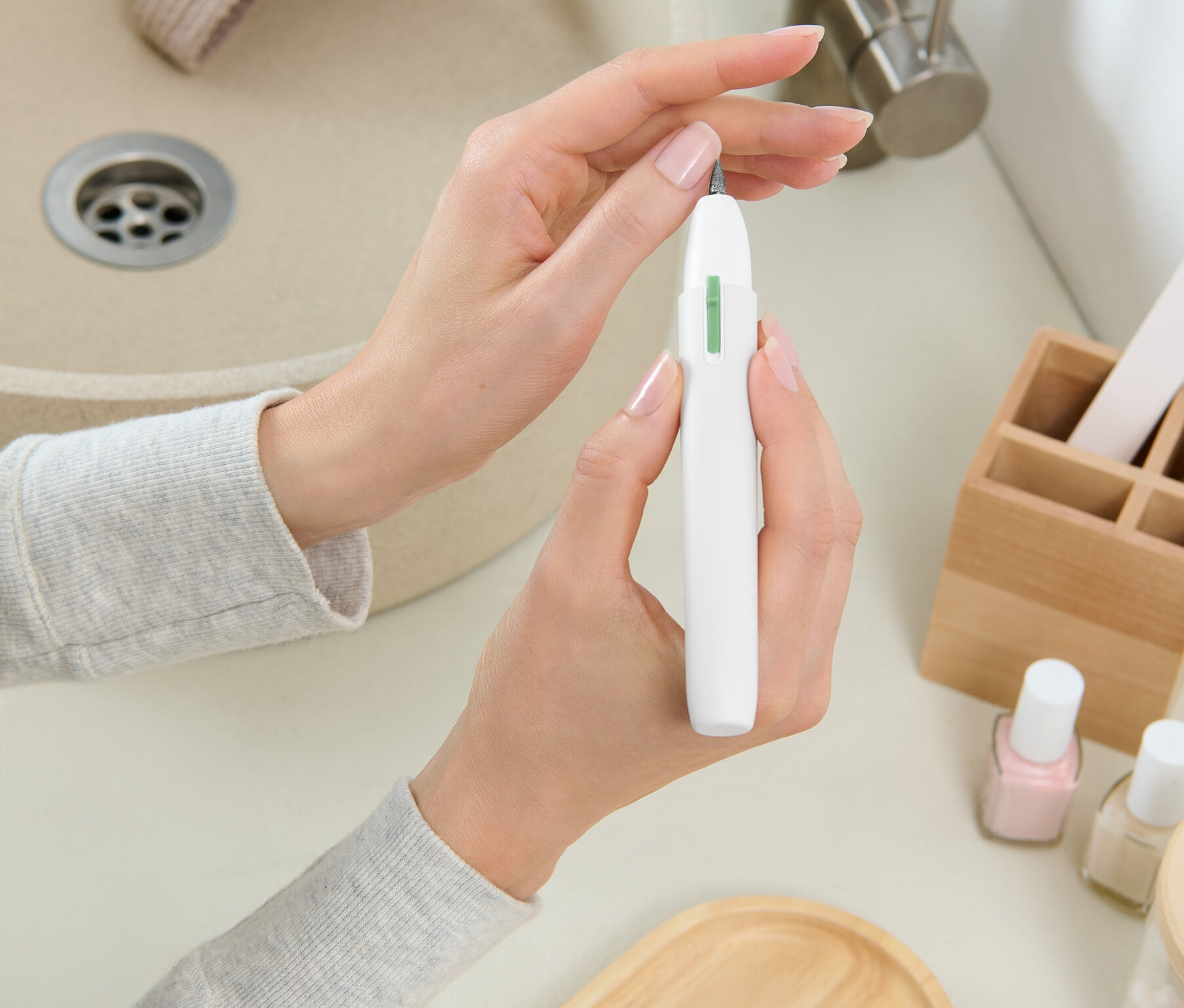 Eine Frau hält einen weißen Nagelfräser vor einem Waschbecken.