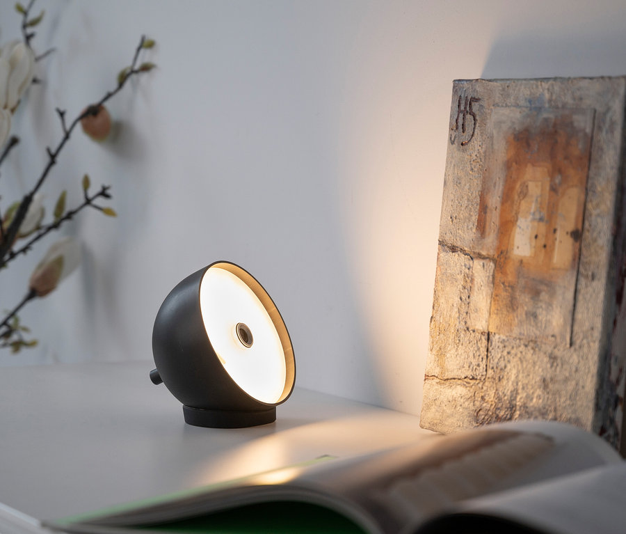 Eine schwarze Lampe steht auf einem weißen Tisch neben einem aufgeschlagenen Buch.