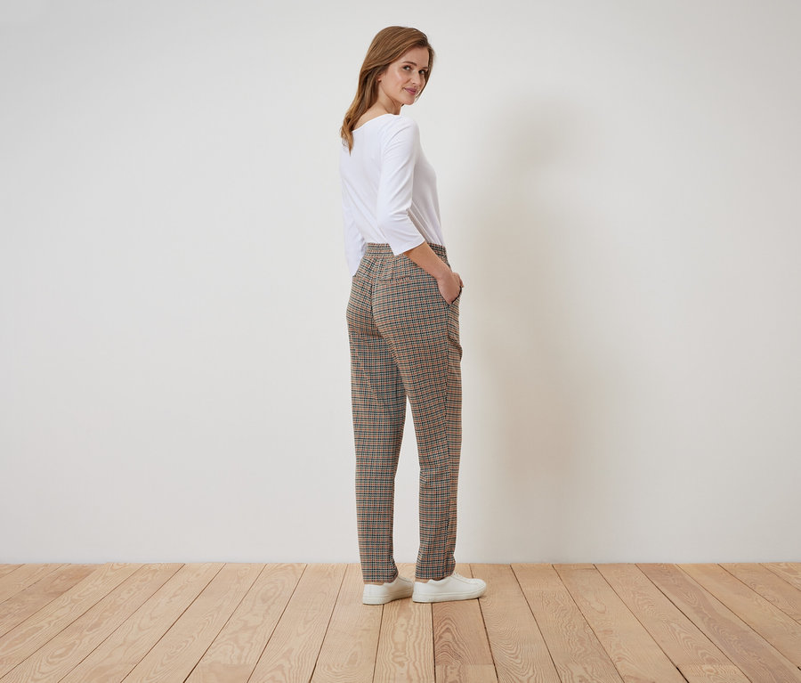 Frau posiert in karierter Hose und weißem Oberteil.