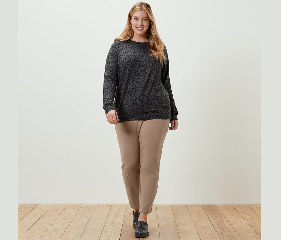 Frau trägt ein bedrucktes Fledermausshirt und eine beige Joggpants und geht.