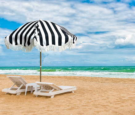 Sandstrand mit zwei weißen Liegestühlen und einem kleinen Tisch unter einem schwarz-weiß gestreiften Leco Strand-Sonnenschirm.