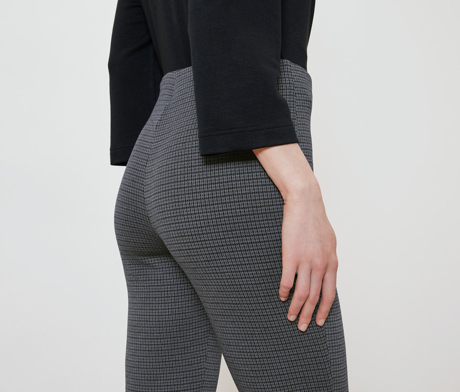 Detailaufnahme einer Frau, die gemusterte Hosen und eine schwarze Bluse trägt.