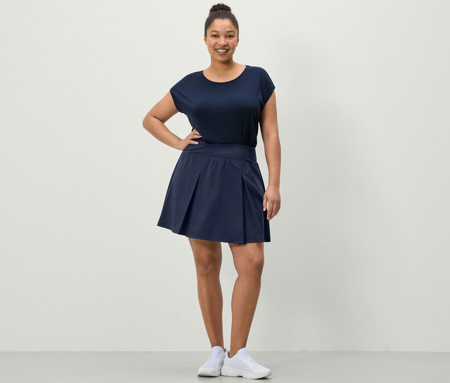 Frau posiert in einem dunkelblauen Sportrock und einem blauen Sportshirt.