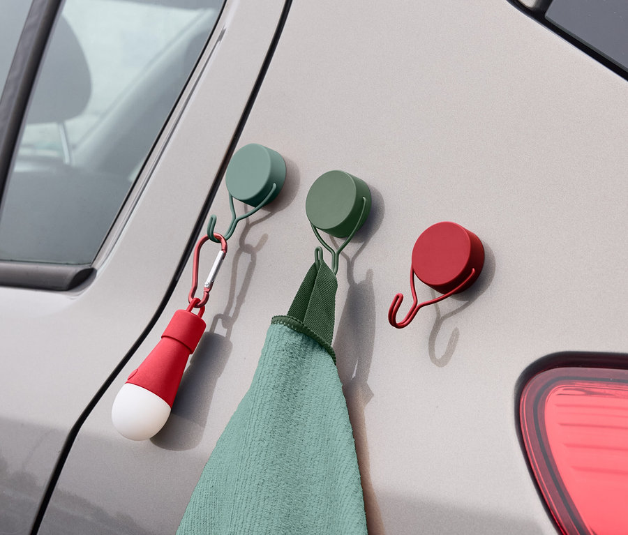 An der Seite eines Autos hängen drei farbige Haken, an denen ein Handtuch und eine Lampe befestigt sind.