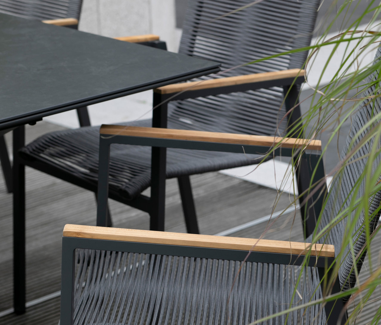 Nahaufnahme eines grauen Gartentisches und Stühle mit Holzarmlehnen.