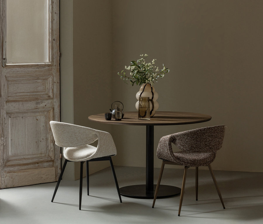 Zwei »Yossi« Esszimmerstühle mit Metallfuß in Kupferbraun stehen an einem runden Holztisch mit Blumenvase.