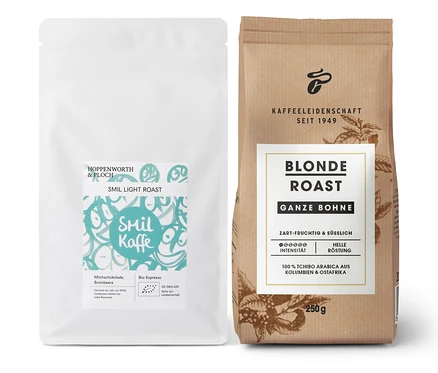 Eine weiße Packung Smil Kaffe Light Roast und eine braune Packung Blonde Roast Kaffee, ganze Bohne, stehen nebeneinander.