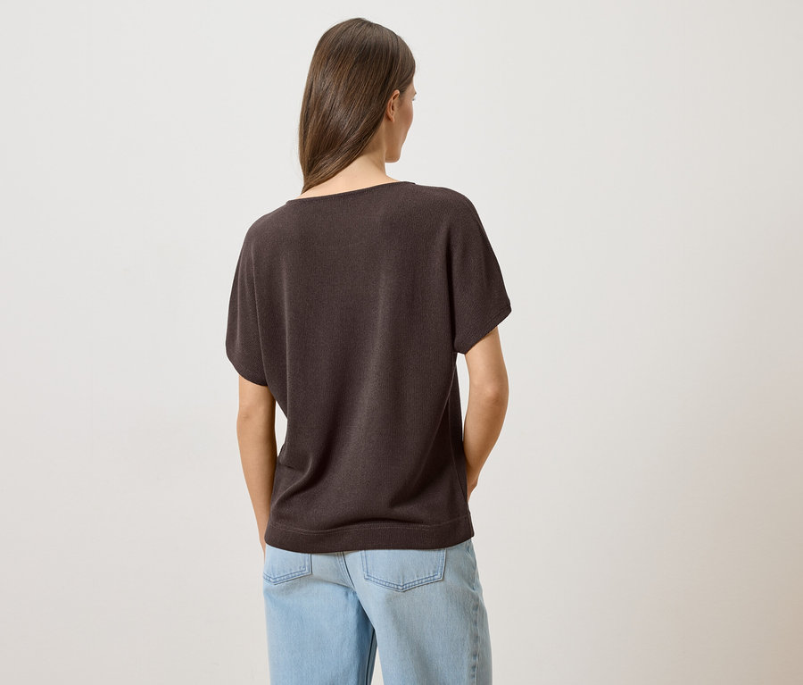Rückansicht einer Frau mit braunen Haaren, die ein braunes T-Shirt und hellblaue Jeans trägt.