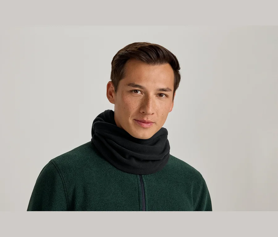 Mann trägt einen schwarzen Halswärmer und ein dunkelgrünes Oberteil mit Reißverschluss und blickt lächelnd in die Kamera.