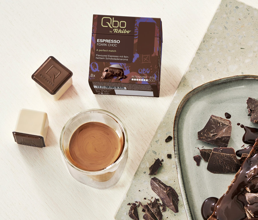 Ein Stück Schokoladentarte mit Qbo Flavoured Espresso Dark Choc Kapseln und Espresso in einem Glas.