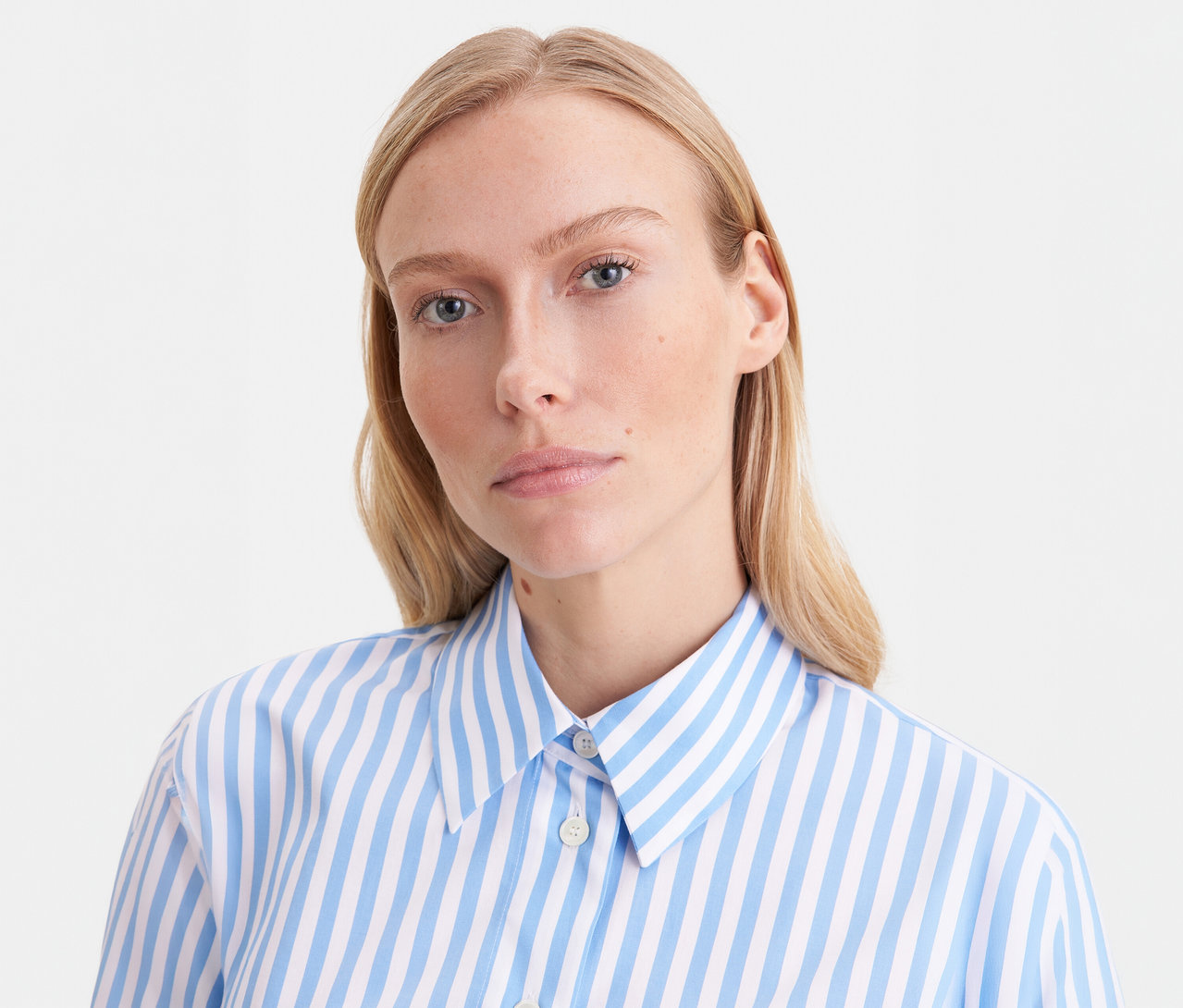 Blonde Frau trägt eine blau-weiß gestreifte Seidensticker Oversize Hemdbluse und blickt in die Kamera.