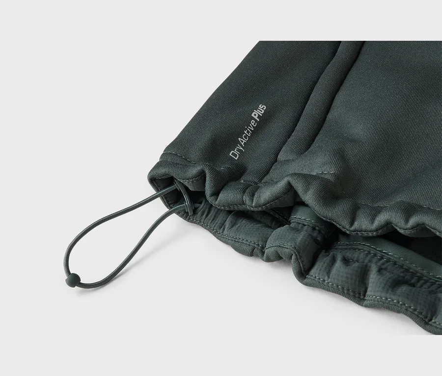 Nahaufnahme eines dunkelgrünen Stoffes, möglicherweise Sportbekleidung, mit einem Kordelzug und dem Text „DryActive Plus“. Der Stoff ist um den Kordelzug gerafft, der einen dunklen Stopper hat und eine Schlaufe bildet.