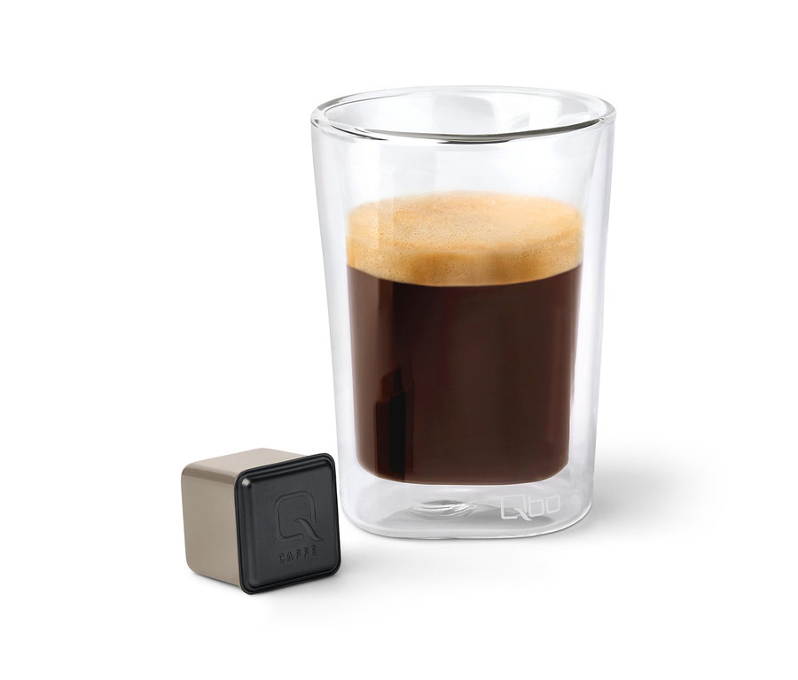 Kaffee in einem transparenten Glas neben einer Qbo Caffè Kapsel.