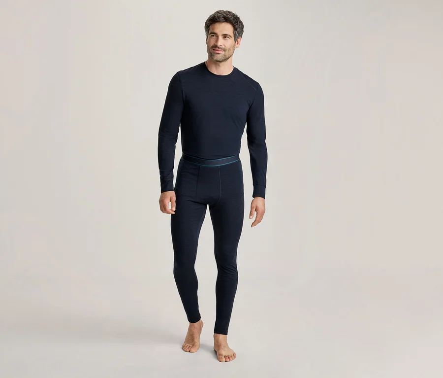 Mann in dunkelblauem, langärmeligem Thermoshirt und passender Thermoleggings, barfuß stehend und leicht lächelnd.