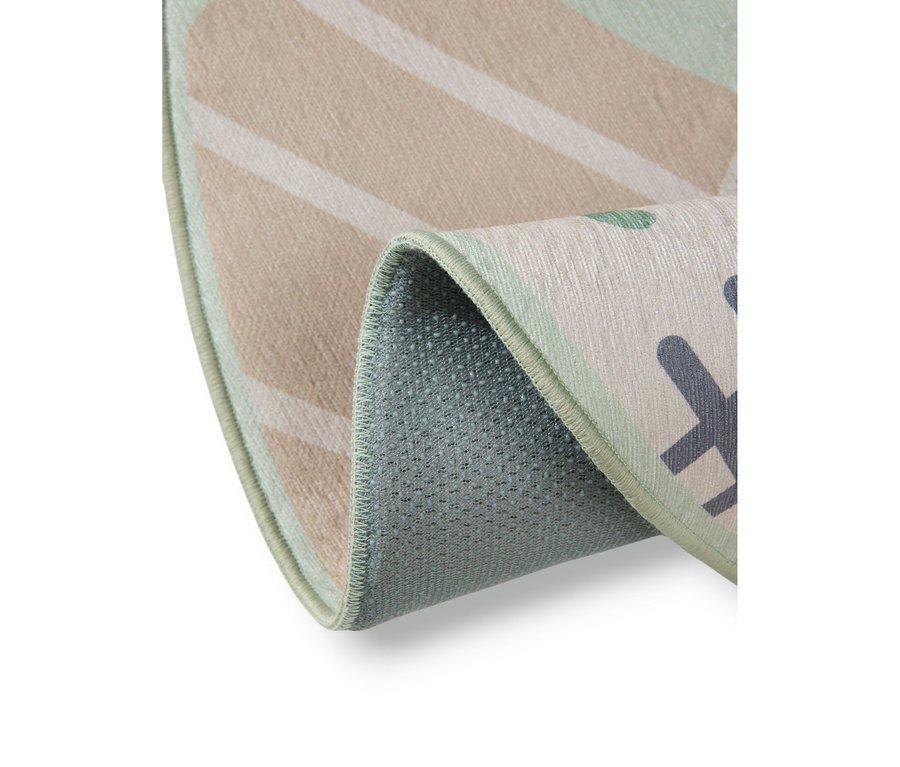 Nahaufnahme eines teilweise gefalteten Teppichs. Die Oberseite zeigt beige diagonale Streifen auf hellbeigem Hintergrund, übergehend in einen hellgrünen Bereich mit dunkelgrauen geometrischen Formen und grünen Punkten. Der Teppich hat eine hellgrüne Umrandung, und seine texturierte, hellblau-grüne Unterseite ist sichtbar.
