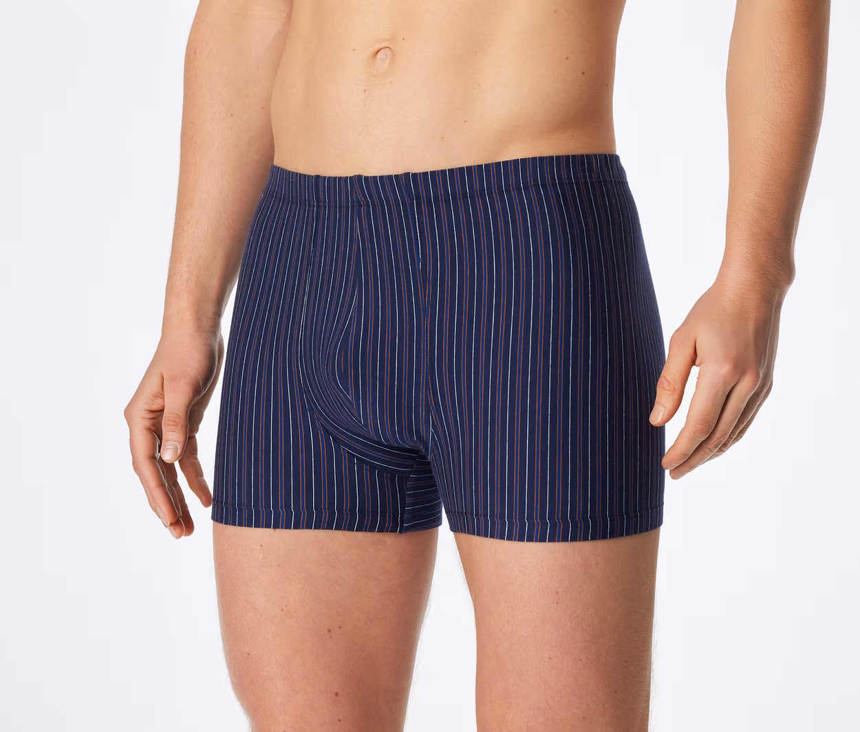 Oberkörper und Oberschenkel eines Mannes, der marineblaue Boxershorts mit dünnen weißen und roten Längsstreifen trägt.