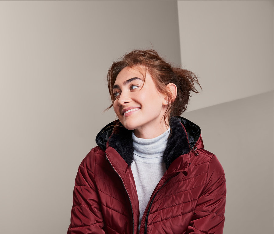 Frau sitzt und trägt eine Steppjacke.