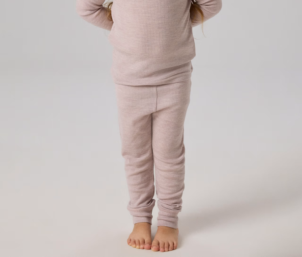 Kind steht barfuß in einem hellrosa gerippten Langarmshirt und passenden Leggings.
