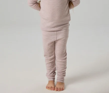 Kind steht barfuß in einem hellrosa gerippten Langarmshirt und passenden Leggings.