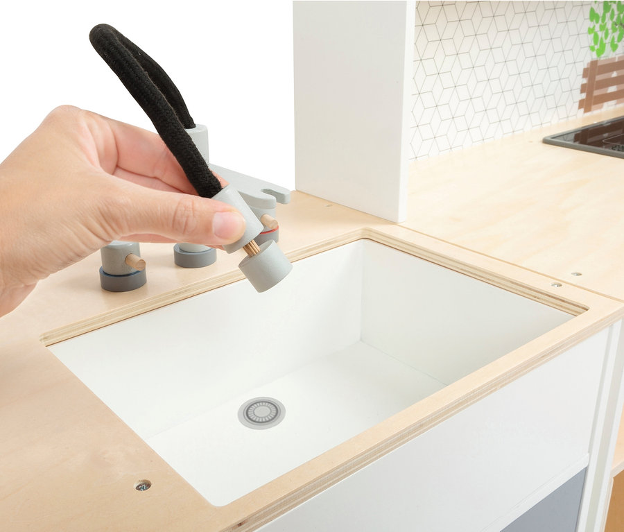 Eine Hand hält einen Wasserhahn über ein Spülbecken in einer small foot Kinderküche modular XL.