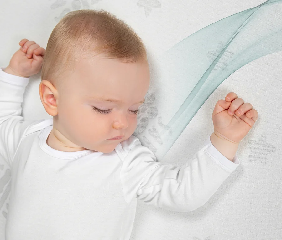 Schlafendes Baby in einem weißen Langarm-Body auf einer Matratze mit Sternenmuster und blauen Wellen.