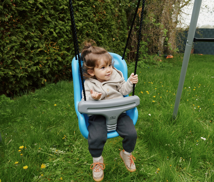 Ein Kind sitzt in einer blauen HUDORA Baby-Hochschaukel im Garten.