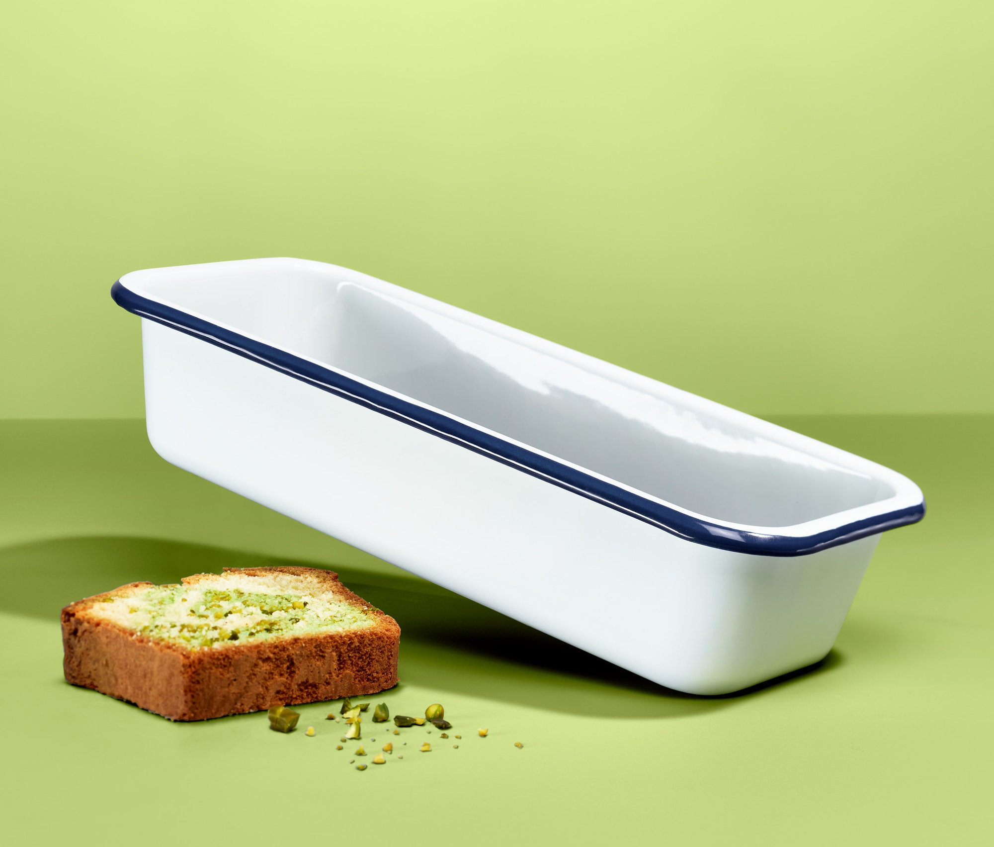 Schwebende Emaille-Kastenform neben einem Stück Kuchen auf grünem Hintergrund.