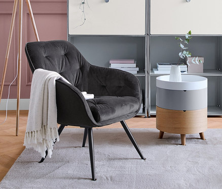 Wohnzimmer mit grauem Regal, Sessel und »Dreibein« Stehleuchte aus Holz.