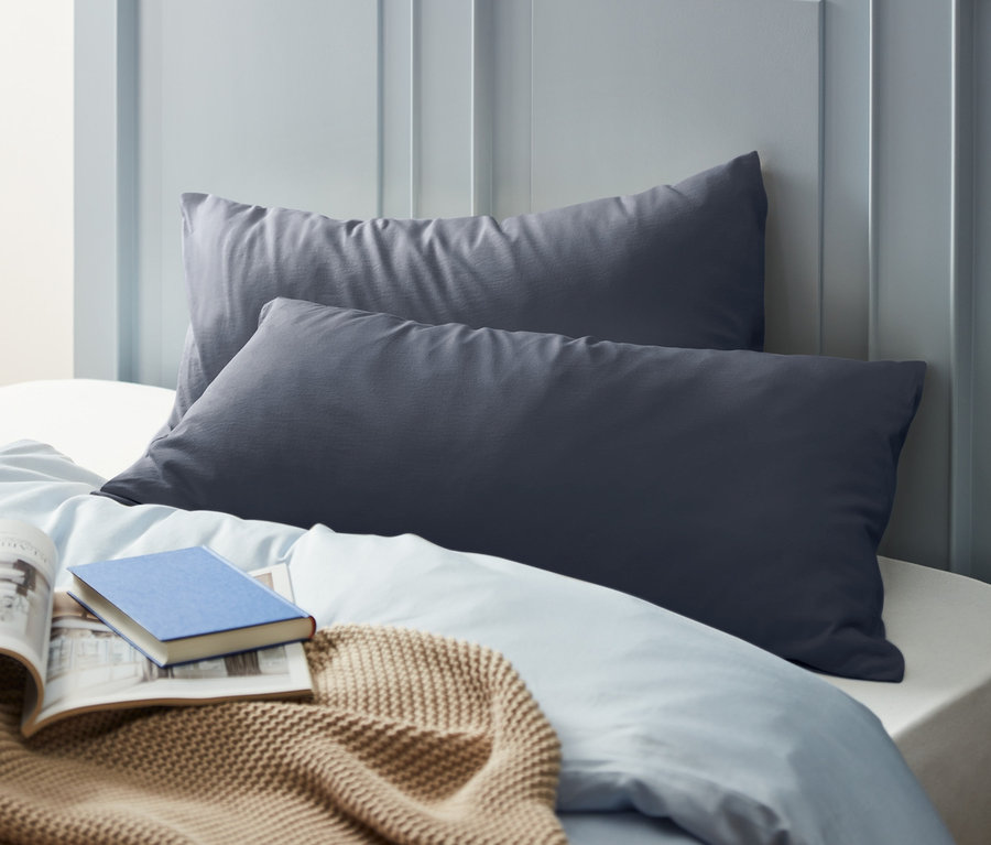 Zwei blaue Jersey-Kopfkissenbezüge (je ca. 80 x 40 cm) liegen auf einem Bett mit einem Buch und einer beigen Decke.