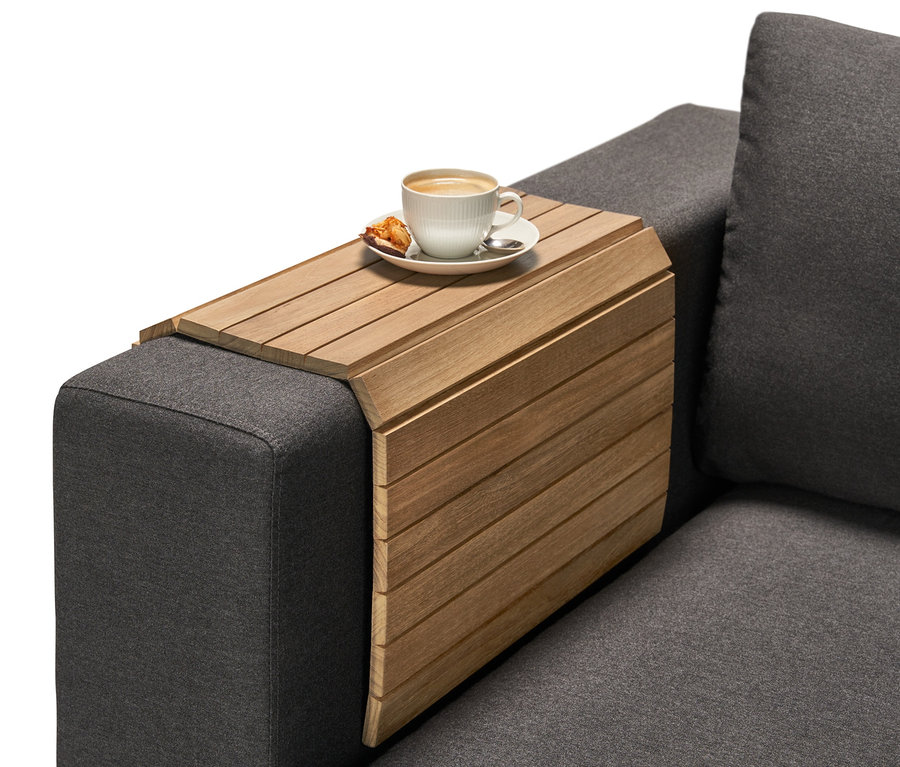 Eine Tasse Kaffee und ein kleines Gebäckstück stehen auf einem Teak-Sofatablett mit Lamellen auf der Armlehne eines grauen Sofas.